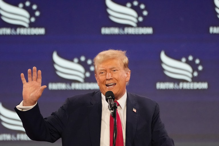 Donald Trump waves as he speaks into a microphone