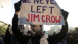 A protester holds up a sign that reads "We Never Left Jim Crow" during a protest.