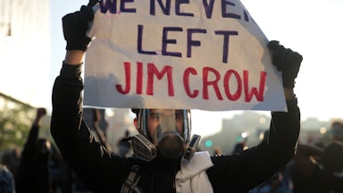 A protester holds up a sign that reads "We Never Left Jim Crow" during a protest.