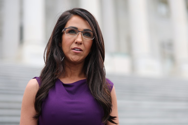 Lauren Boebert wears a purple dress and glasses and looks off camera. She may be standing on the steps of the Capitol.