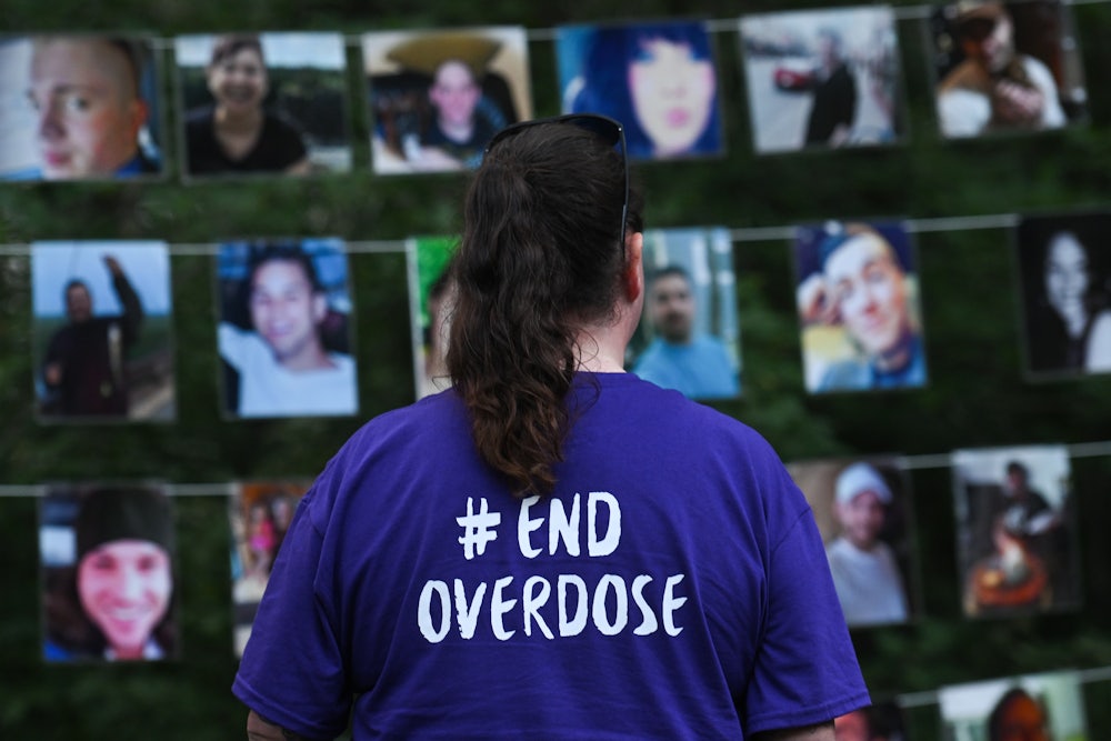 A woman wearing a shirt that reads "End Overdose" looks at photos of those lost to drug overdoses.