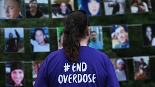 A woman wearing a shirt that reads "End Overdose" looks at photos of those lost to drug overdoses.