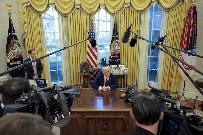 President Donald Trump talks to reporters from the Resolute Desk after signing an executive order.