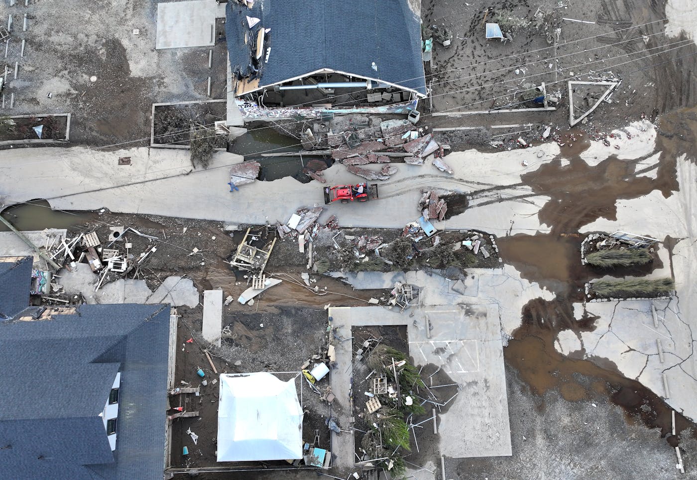 An aerial photo shows a person in a front-end loader driving through wreckage between buildings.