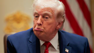 Donald Trump makes a puckering expression while wearing a blue suit and red tie.