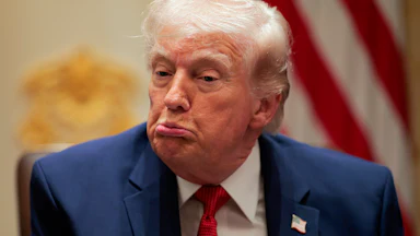 Donald Trump makes a puckering expression while wearing a blue suit and red tie.