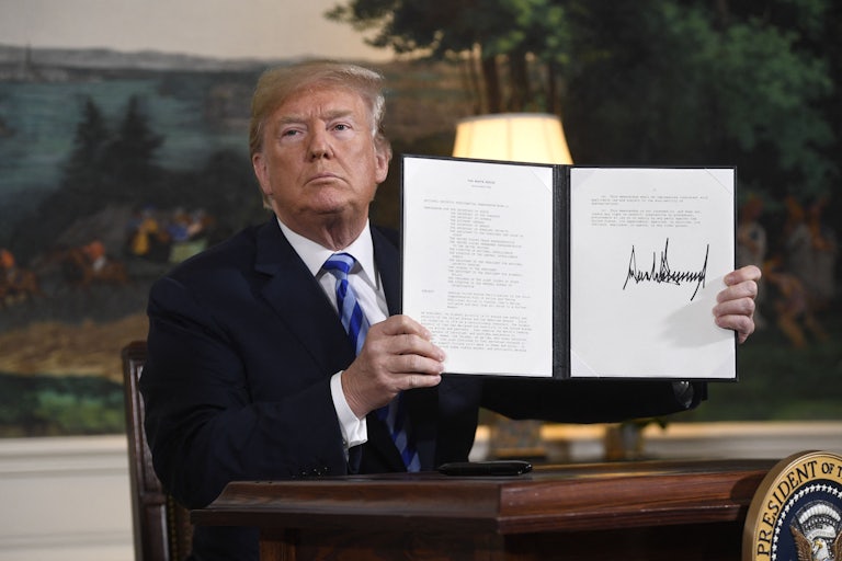 Donald Trump sits behind a desk, holding a signed executive order.