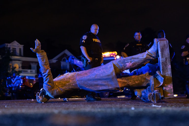 Police officers look at a toppled Confederate statue.