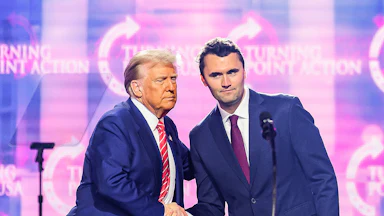 Donald Trump and Charlie Kirk shake hands while standing on stage during a Turning Point USA event