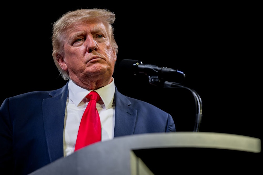 Former President Donald Trump speaks in front of a black background, with a microphone in front of him