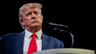 Former President Donald Trump speaks in front of a black background, with a microphone in front of him