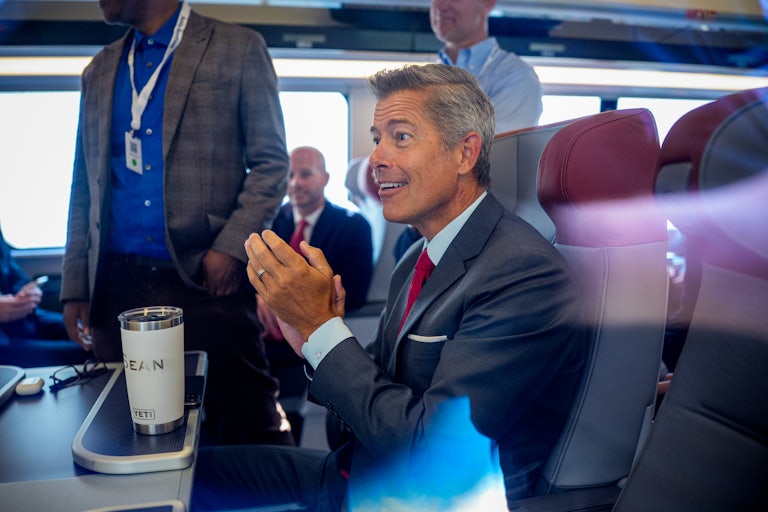 Transportion Secretary Sean Duffy claps while sitting on a train.