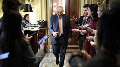 Chuck Schumer walks between reporters holding out phones.