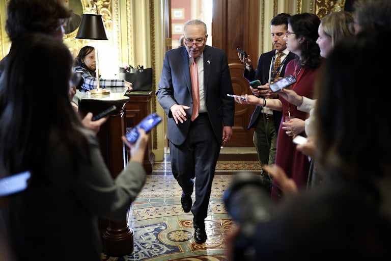 Chuck Schumer walks between reporters holding out phones.