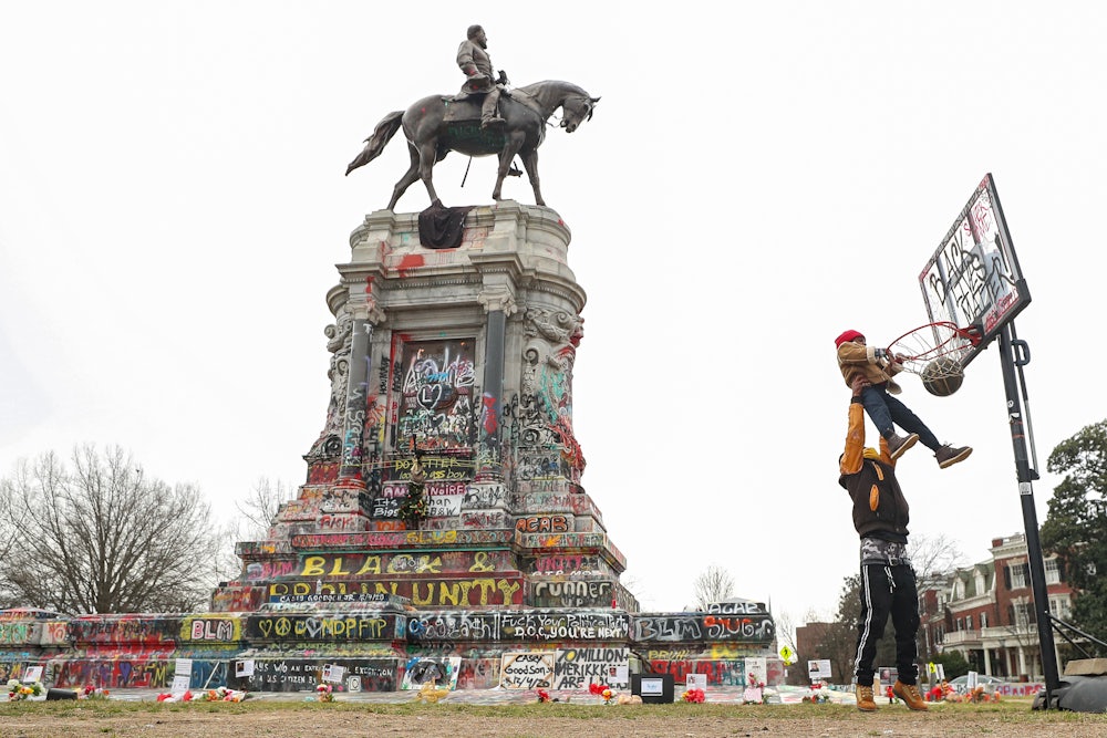A man lifts his son to dunk a basketball in front of a defaced statue of Robert E. Lee in Richmond, Virginia.