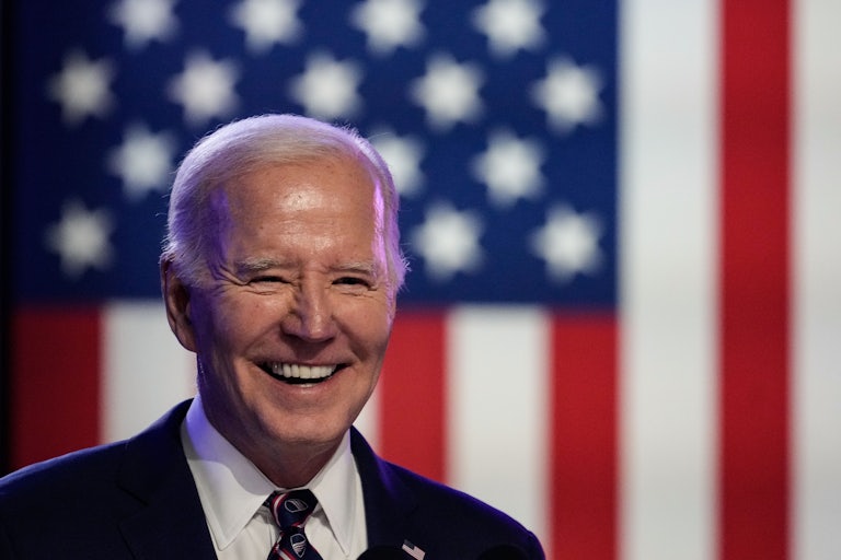 Joe Biden smiles while standing in front of an American flag.
