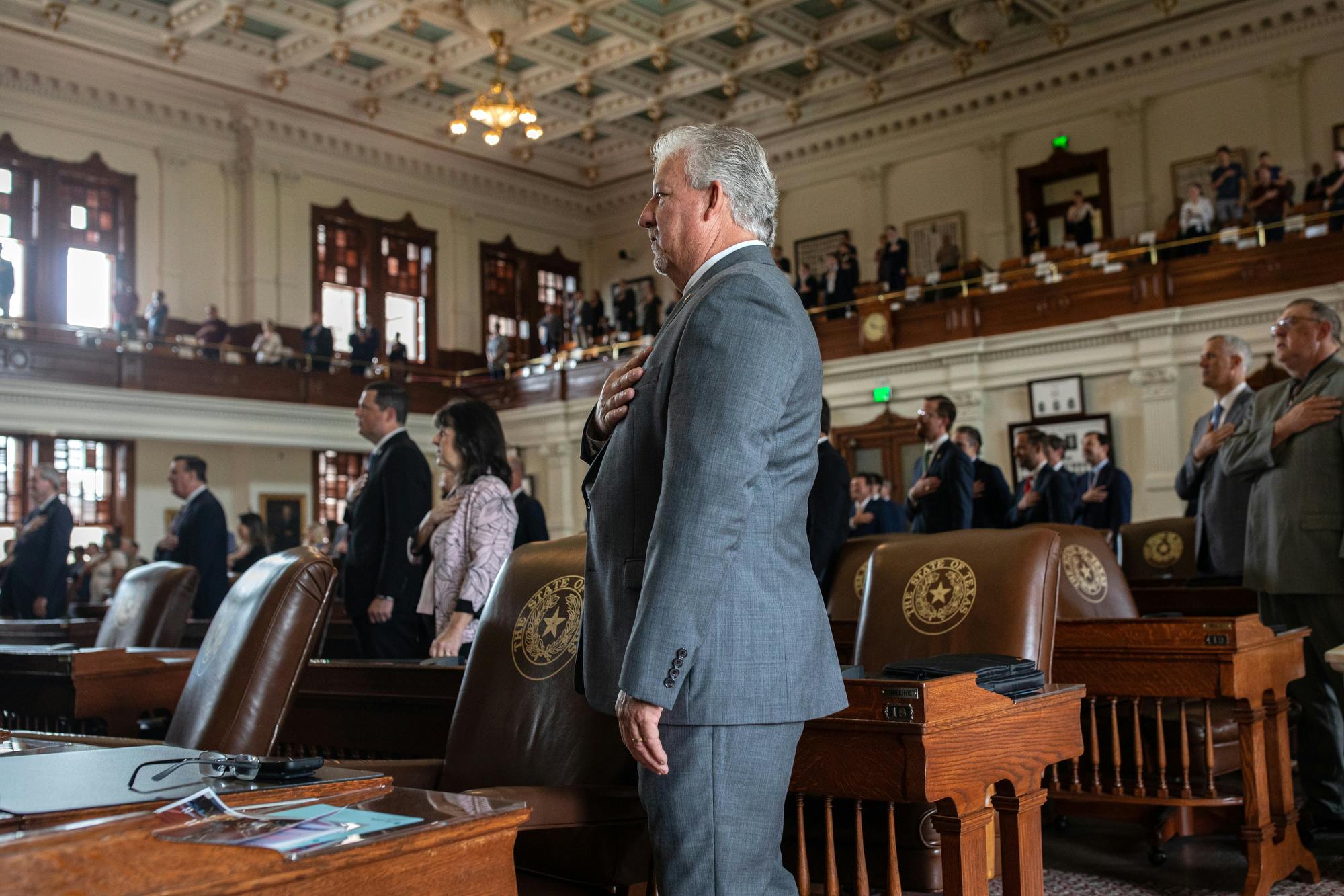 Representatives in suits stand with their hands over their hearts.