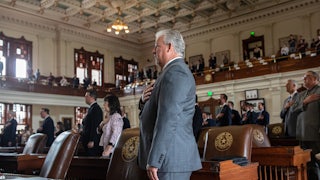Representatives in suits stand with their hands over their hearts.
