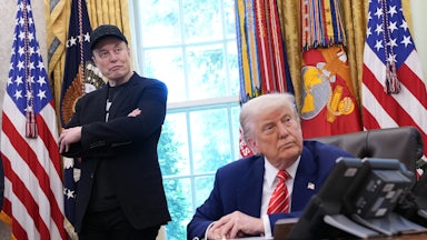 Donald Trump sits at his desk in the Oval Office, while Elon Musk stands behind him with his arms crossed