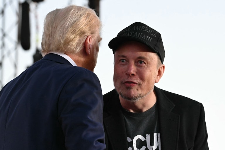 Donald Trump leans forward and says something in Elon Trump's ear