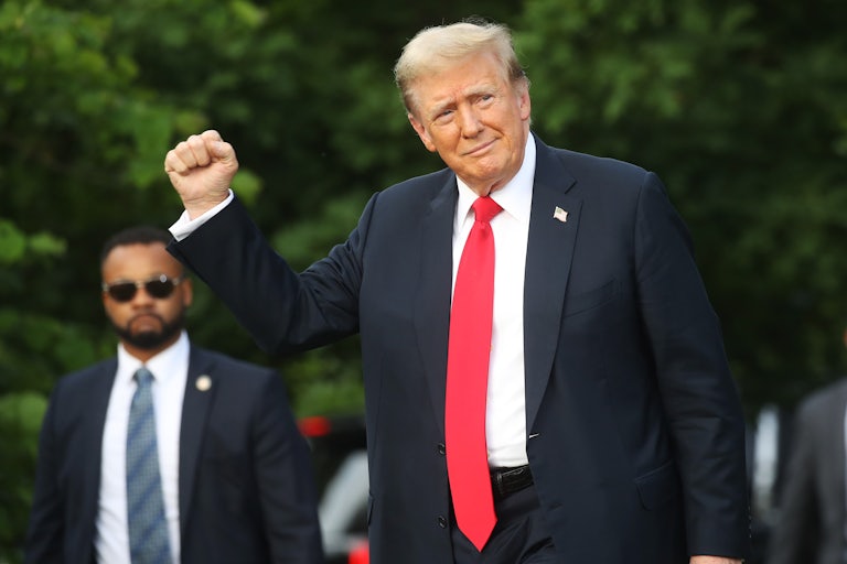 Donald Trump raises his right fist as if in victory. A man who is likely his bodyguard is in the background.