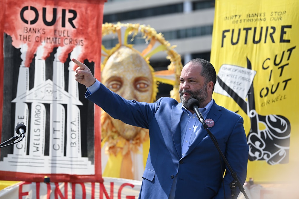 Ben Jealous raises his hand while standing at a microphone in front of posters.