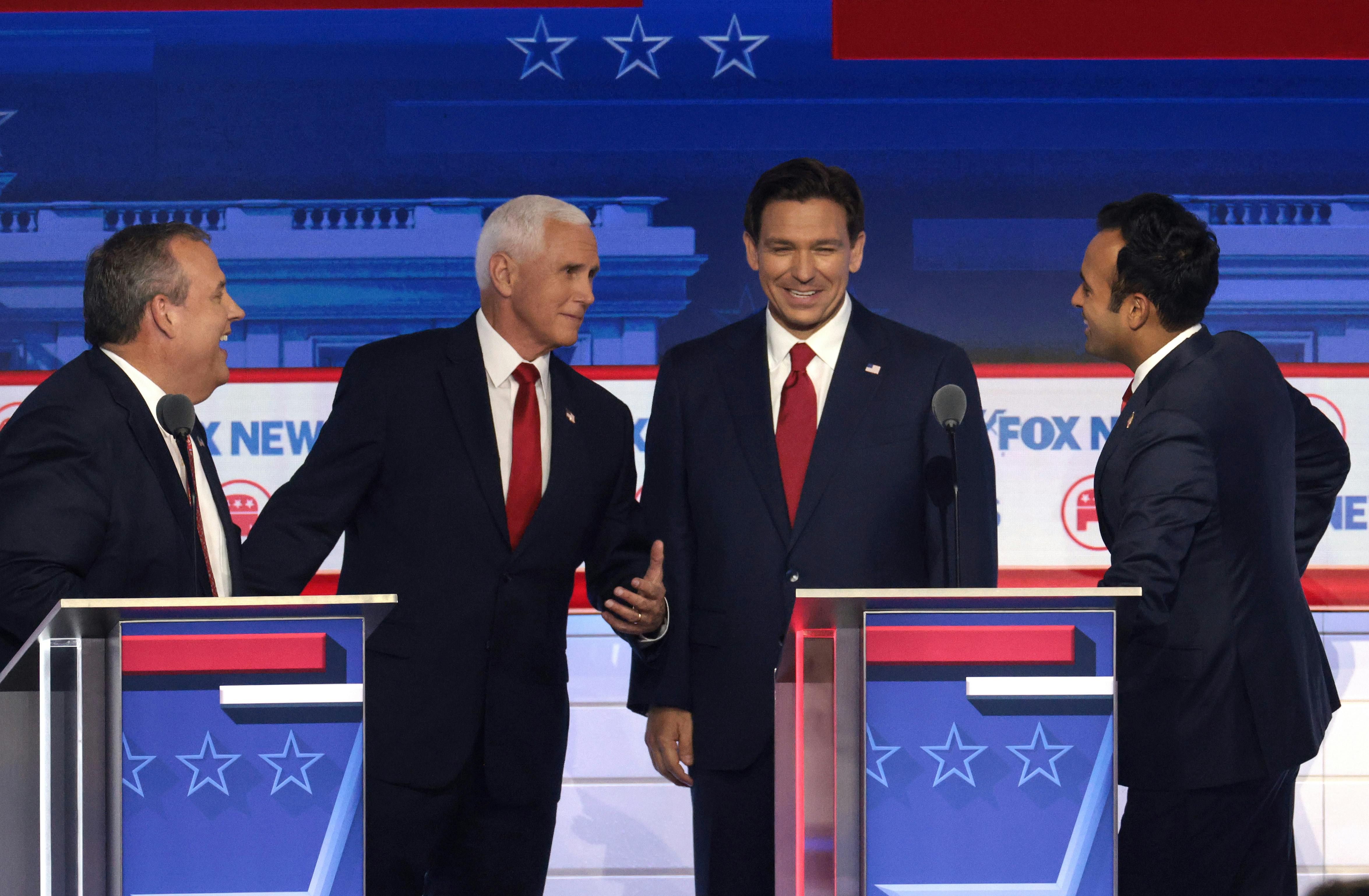 Republican presidential candidates Chris Christie, Mike Pence, Ron DeSantis, and Vivek Ramaswamy share a laught together behind their lecterns at a recent debate.
