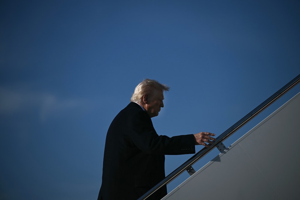 Trump walks up steps against a blue sky.