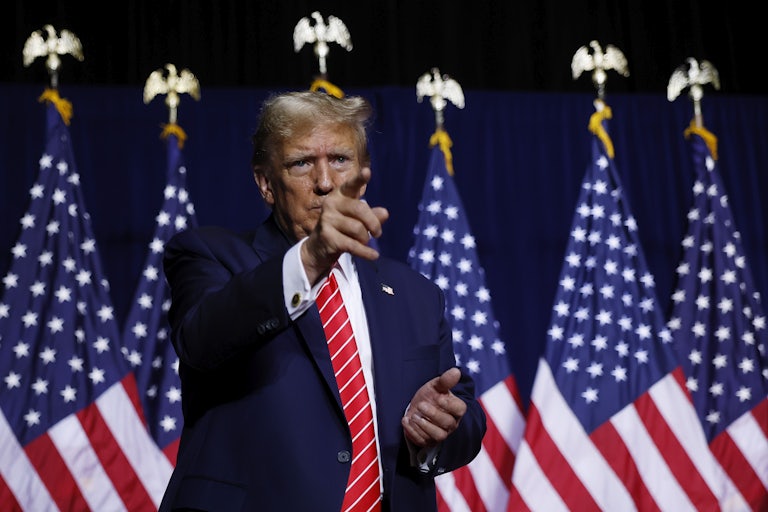 Donald Trump points to the crowd in front of him (not pictured). A row of U.S. flags are behind him.
