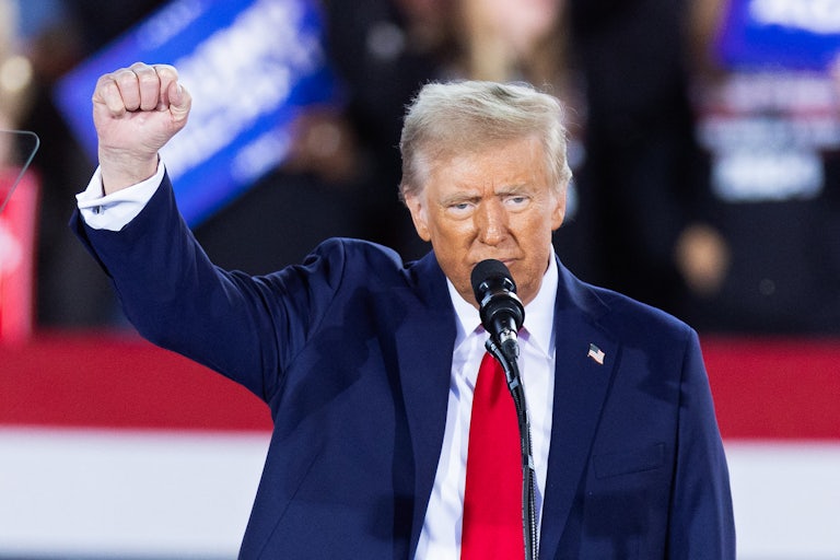 Donald Trump holds up his fist while speaking into a microphone