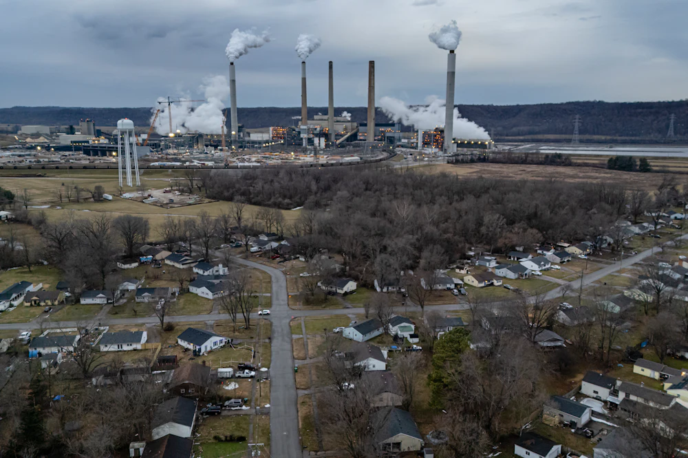 An aerial view shows smokestacks in the background and suburban streets in the foreground.