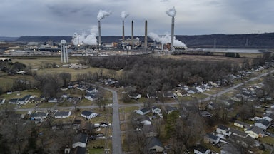 An aerial view shows smokestacks in the background and suburban streets in the foreground.