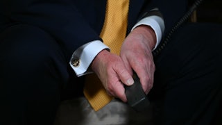 Donald Trump's hands are folded between his knees while he sits. He holds some a phone receiver.