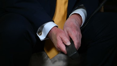 Donald Trump's hands are folded between his knees while he sits. He holds some a phone receiver.
