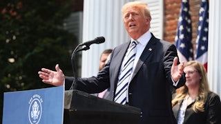 Donald Trump gestures with his hands from behind a podium featuring a sign that reads, "The Office of Donald J. Trump"