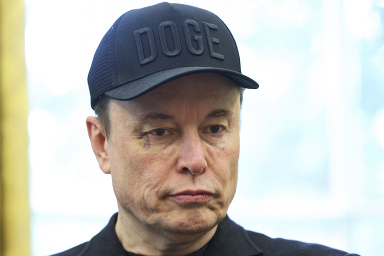 Elon Musk looks down while standing in the Oval Office
