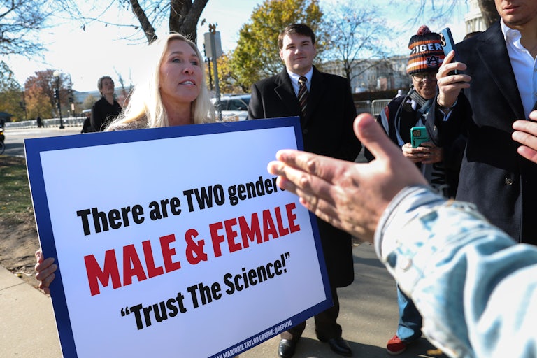 Representative Marjorie Taylor Greene outside the Supreme Court holds a giant sign that reads "There are two genders: Male & Female 'Trust the Science!'"