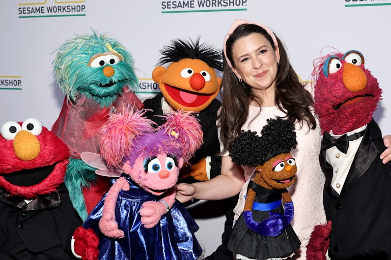 Ms. Rachel smiles along with several Sesame Street puppets.