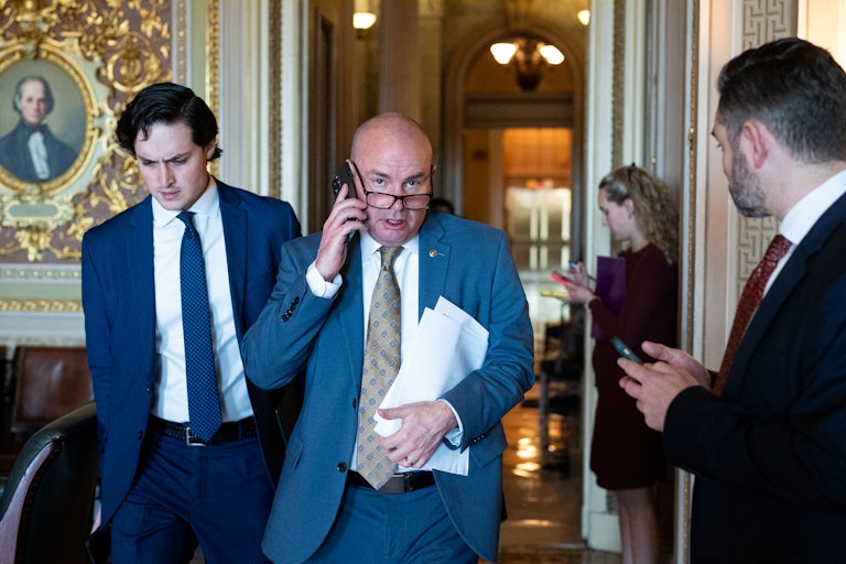 Mike Lee walks through the Capitol holding a phone. He's flanked by an aide