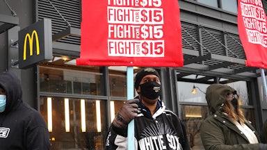 Three masked workers in front of a McDonalds holding red "Fight for 15" signs