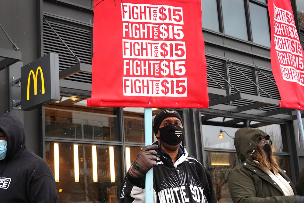 Three masked workers in front of a McDonalds holding red "Fight for 15" signs