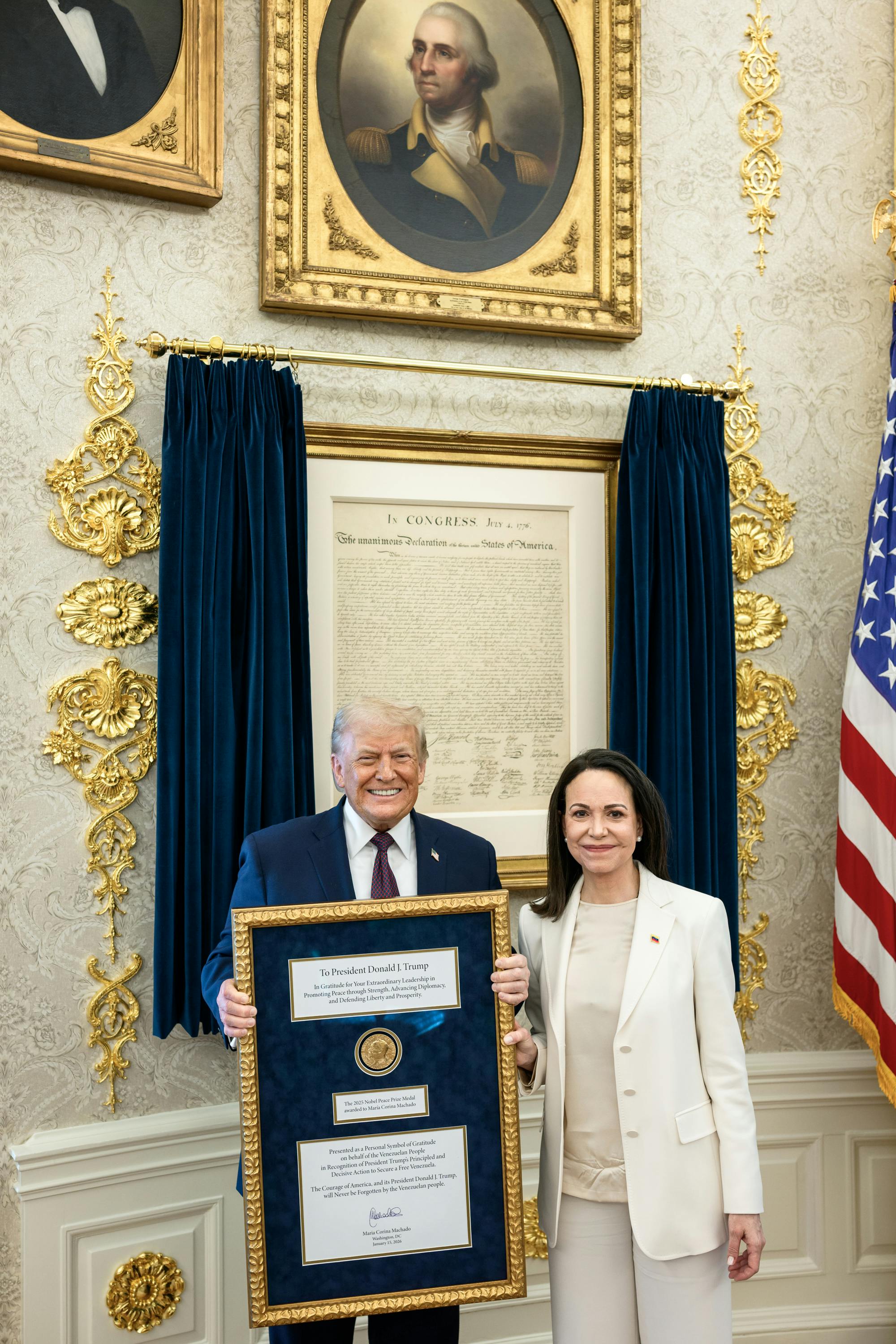 Nobel Peace Prize winner María Corina Machado smiles next to Donald Trump in the Oval Office of the White House, as he holds her framed Nobel Prize.