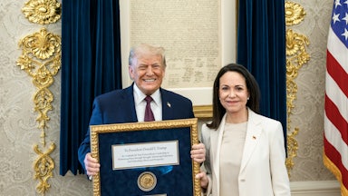 Nobel Peace Prize winner María Corina Machado smiles next to Donald Trump in the Oval Office of the White House, as he holds her framed Nobel Prize.