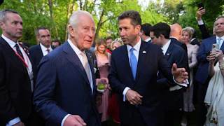 Britain’s King Charles III, drink in hand, and the British Ambassador to the U.S. Christian Turner speak as a group of people surround them.