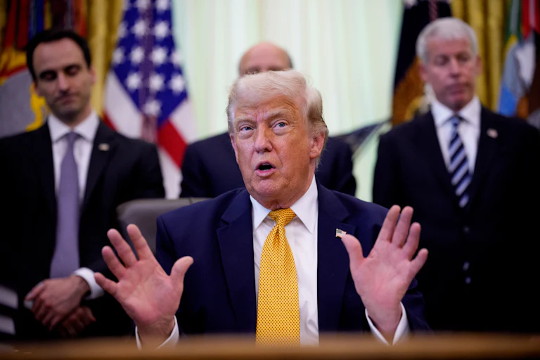Donald Trump speaking at his desk in the Oval Office of the White House, while others stand behind him.