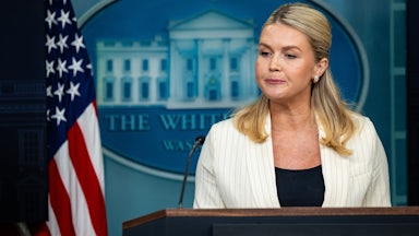 Karoline Leavitt presses her lips together while standing at the podium in the White House press briefing room