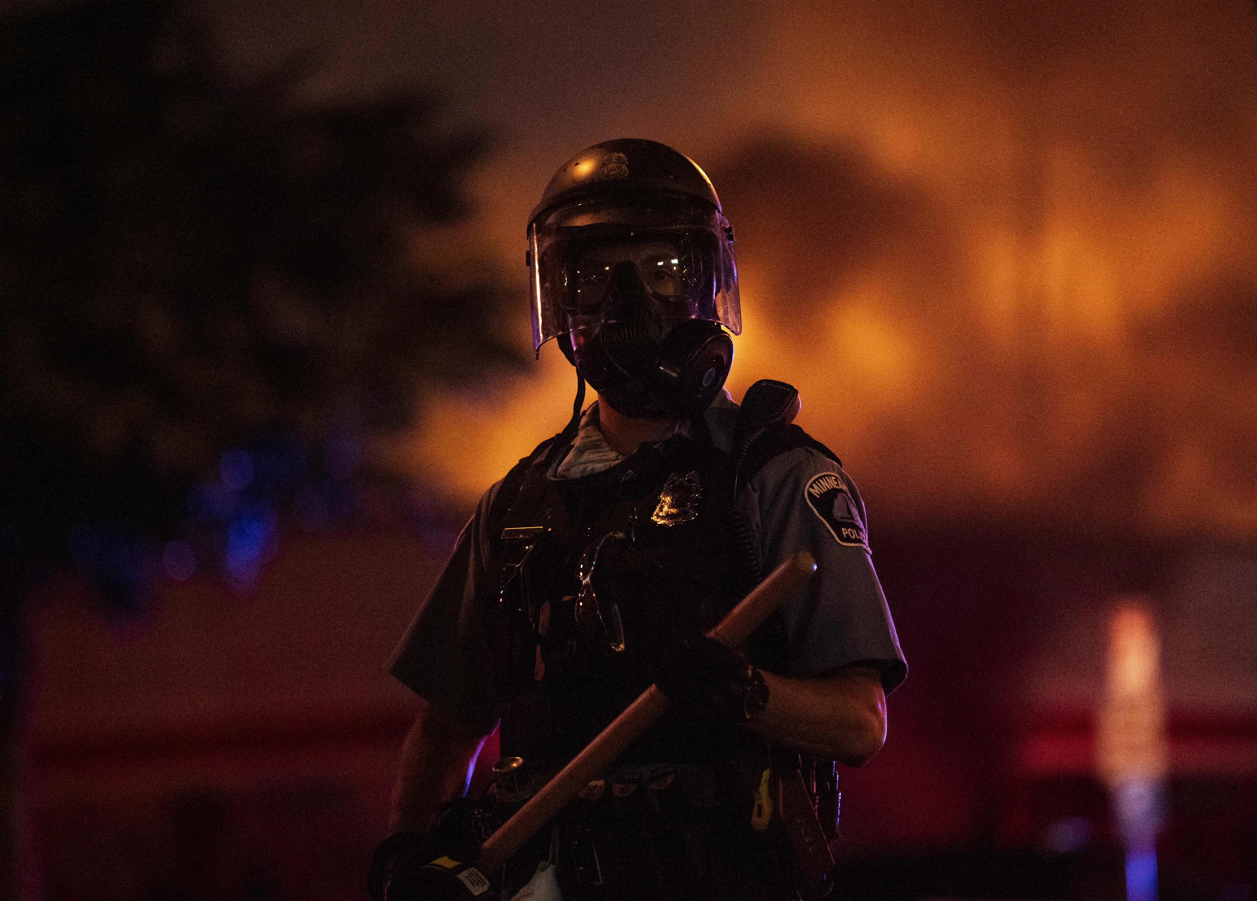 A police officer stands with a baton as a fire burns inside an Auto Zone store in Minneapolis