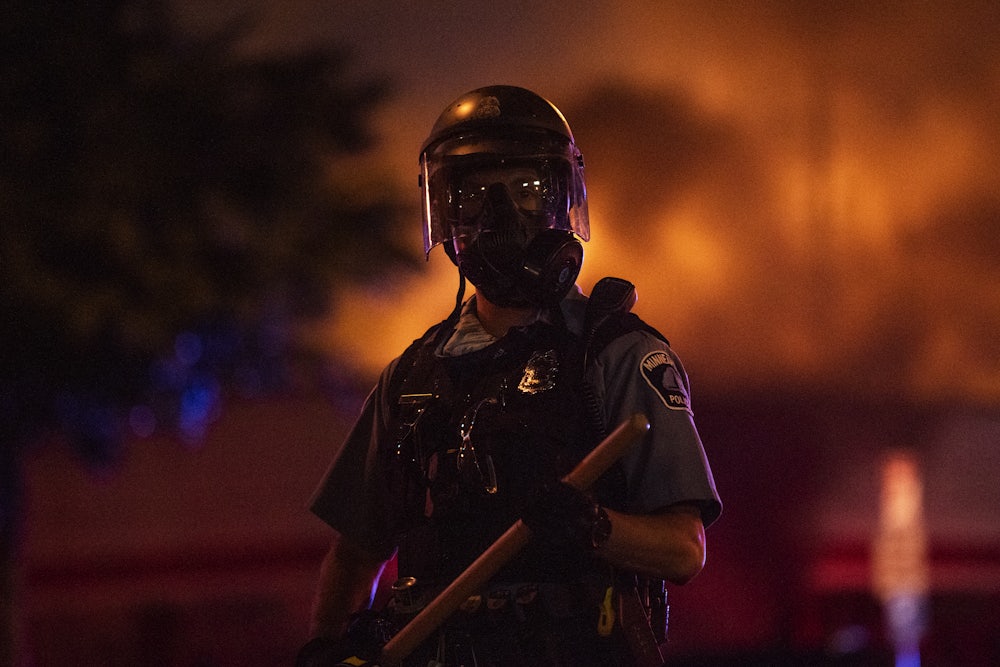 A police officer stands with a baton as a fire burns inside an Auto Zone store in Minneapolis