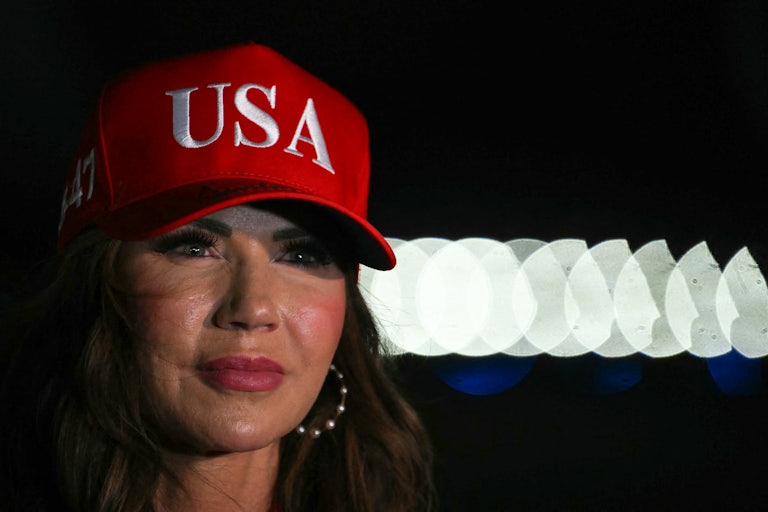 Homeland Security Secretary Kristi Noem wears a "USA" hat and stands on the tarmac at Joint Base Andrews