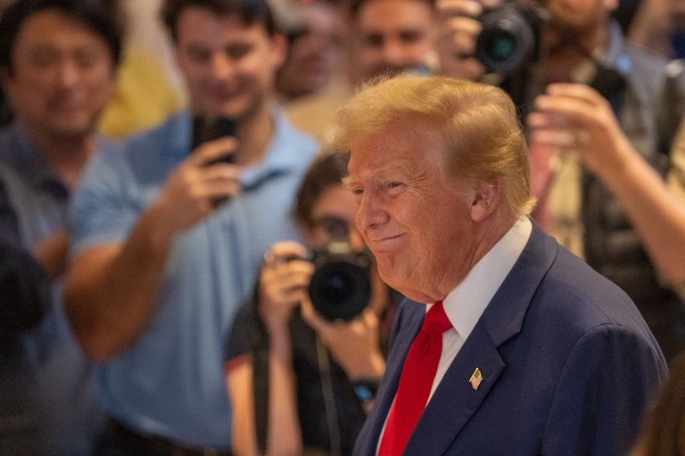 Donald Trump smiles weirdly; a crowd is behind him
